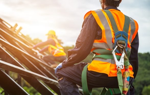 [safety body construction] Working at height equipment. Fall arrestor device for worker with hooks for safety body harness on selective focus. Worker as in construction background.