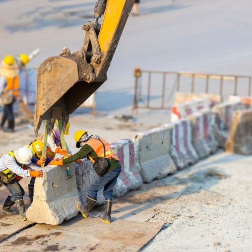 Many workers wear safety suits helped to lift and arrange the cement concrete barriers by excavator In harmony and actively on the road